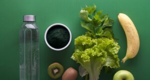 Sortiertes Obst mit Wasser und Gemüse auf grüner Oberfläche