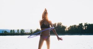 woman in bikini using hoola hoop by shore during golden hour