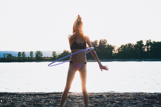 woman in bikini using hoola hoop by shore during golden hour