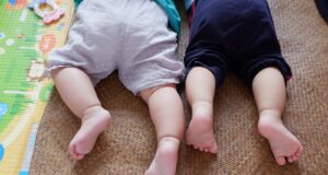 baby in white shirt and black pants lying on brown carpet
