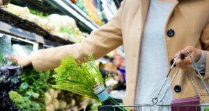 woman in white coat holding green shopping cart