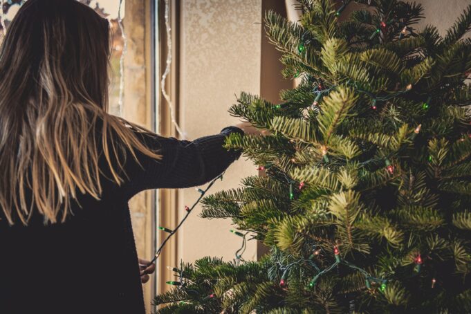 woman installing string lights on Christmas tree