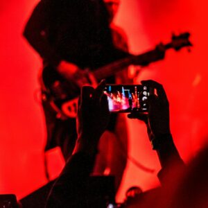 person holding smartphone in front of a person playing guitar on stage
