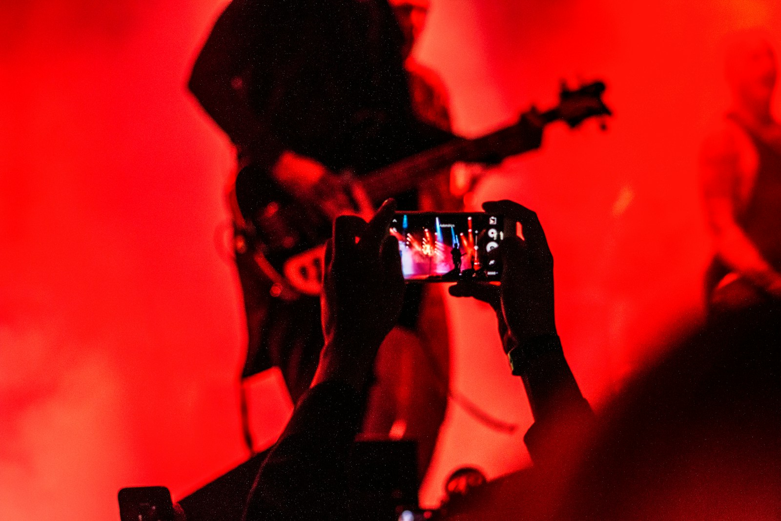 person holding smartphone in front of a person playing guitar on stage