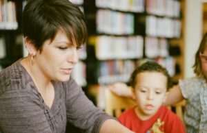 woman in gray long sleeve shirt sitting beside boy in orange crew neck shirt