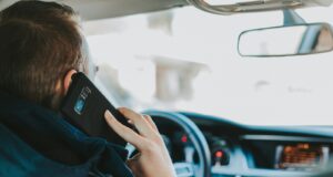 man sitting on car seat front of steering wheel holding phone