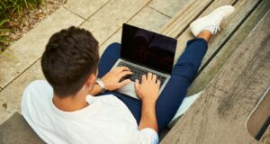 man wearing white sweatshirt using laptop computer sitting on sofa chair