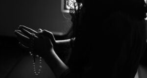 silhouette of woman holding rosary while praying