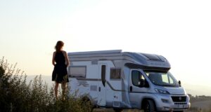woman in black dress standing beside white and blue rv trailer during daytime
