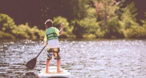 boy riding on surfboard holding black boat oats during daytime