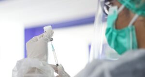 a person in a mask and gloves holding a syringe