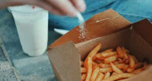 person sprinkling salt in fries