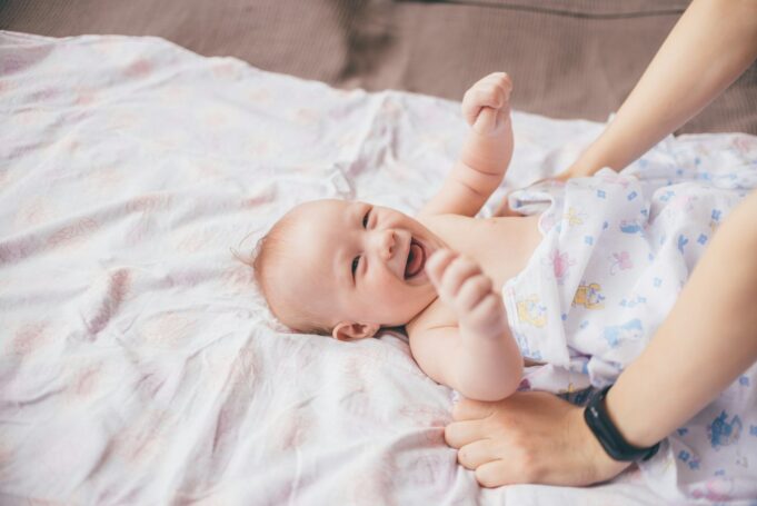 Photo by Daniil Silantev a smiling baby laying on a bed with a woman's arm