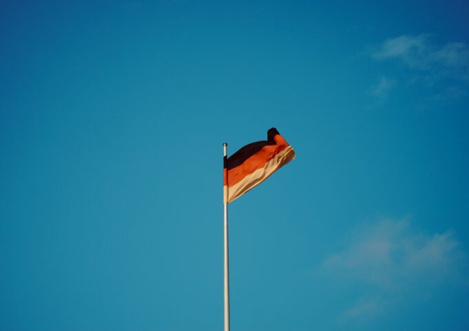 Photo by Viva Zhang red white and yellow flag on pole under blue sky during daytime