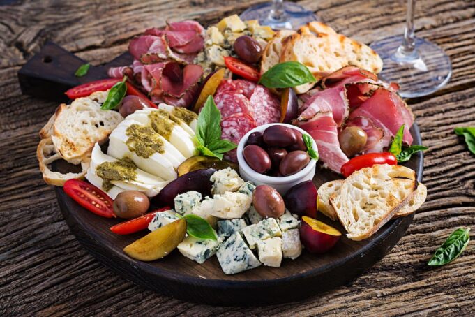 Antipasto platter with ham, prosciutto, salami, blue cheese, mozzarella with pesto and olives on a wooden background.