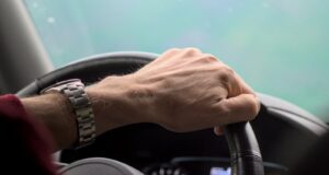 Hand gripping a steering wheel while driving.