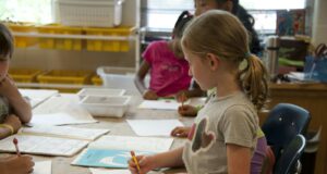 girl in green crew neck t-shirt writing on white paper