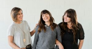 3 women smiling and standing beside white wall