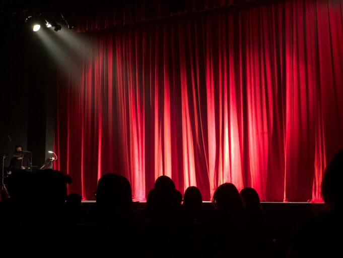 Theater Bühne Dimly lit theater stage with red curtains and audience silhouettes under spotlights.